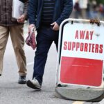 Football fans walk past an away supporters sign